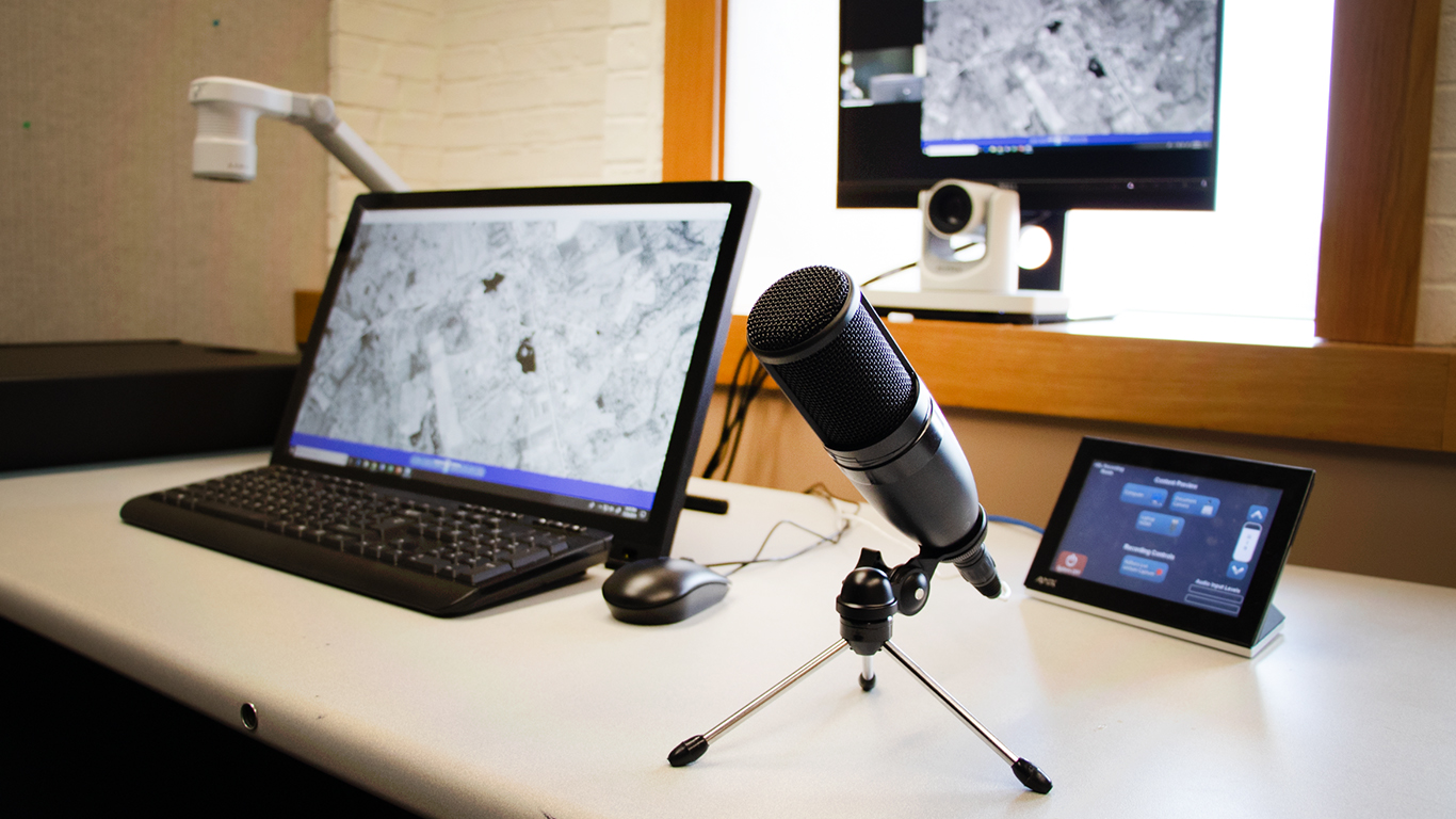 Photo of a computer, microphone, document scanner, camera, and touch screen device on the desk in the One Button Studio